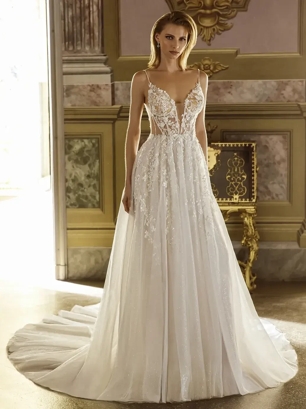 Model is wearing a sleeveless a-line tulle bridal gown with a lace bodice and plunging neckline 